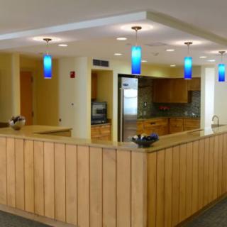 A modern reception area with wood paneling, blue pendant lights, and an adjacent kitchen space.