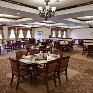 Elegant dining room with neatly arranged tables and chairs, featuring chandeliers and large windows.