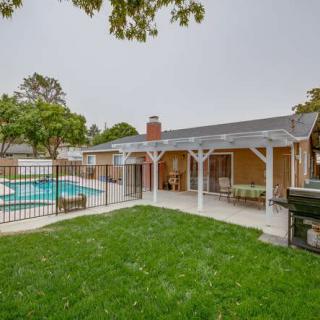 A backyard with a swimming pool and patio area, surrounded by a fence and lush greenery.