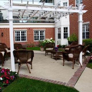 A cozy outdoor patio with wicker chairs and a pergola, surrounded by a well-maintained garden.
