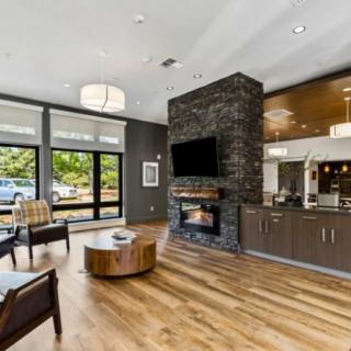 Modern living room with a stone fireplace, wood flooring, and large windows providing natural light.