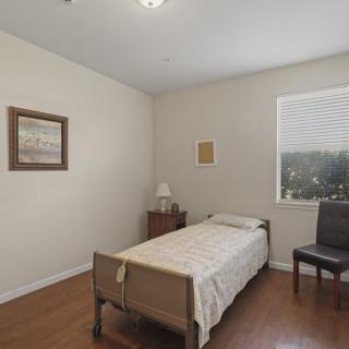 A minimalist bedroom with a single bed, nightstand, chair, and wall art.