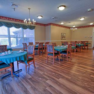 A spacious dining room with neatly arranged tables and chairs, featuring elegant chandeliers and large windows with curtains.