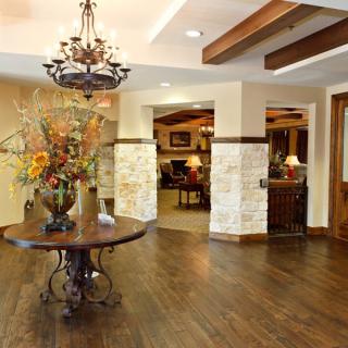 A warmly decorated lobby area featuring a central table with floral arrangements, a chandelier, and wooden flooring.