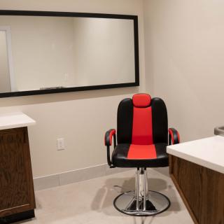 An empty barbershop or hair salon with a stylish red and black barber chair in front of a large mirror.
