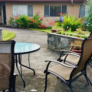 A cozy patio area with chairs and a table, surrounded by a lush garden.