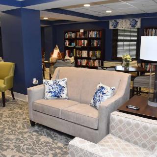 A cozy living room featuring a sofa, armchairs, and bookshelves filled with books.