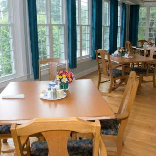 A cozy dining area with wooden tables and chairs, bathed in natural light from large windows.