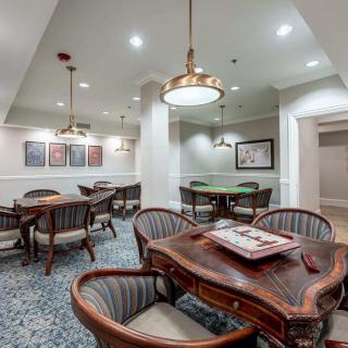 A cozy game room featuring a poker table and elegant seating arrangements, with soft lighting and decorative artwork on the walls.