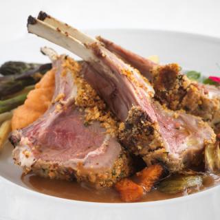 A gourmet rack of lamb served with vegetables.