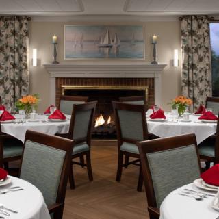 An elegant dining room with round tables set for a formal dinner, featuring a cozy fireplace.