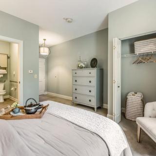 A cozy bedroom with soft lighting, featuring a neatly made bed, dresser, and open closet.