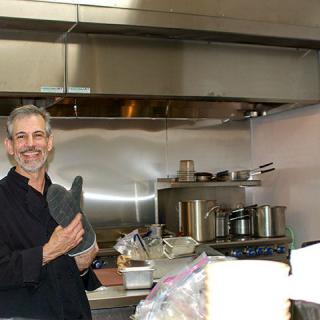 A chef smiling while holding a piece of kitchen equipment in a restaurant kitchen.