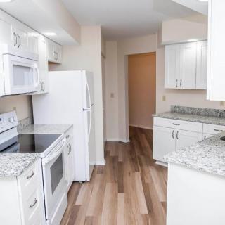 A modern kitchen with white cabinets, granite countertops, and hardwood flooring.