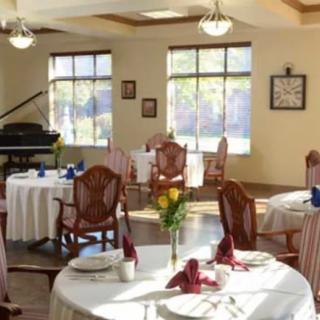 An elegant dining area with round tables, wooden chairs, and a piano by the window.