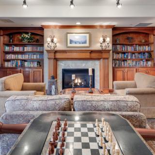 A cozy living room with a fireplace, surrounded by bookshelves and featuring a chess board.