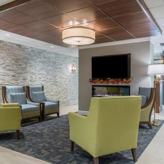 A modern lobby area with comfortable seating, a stone accent wall, and a cozy fireplace below a television.