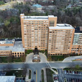 An aerial view of a large residential building surrounded by green trees and a parking area.