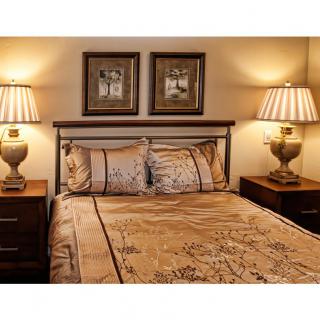 A cozy bedroom featuring a neatly made bed flanked by two nightstands with matching lamps and decorative artwork above the headboard.