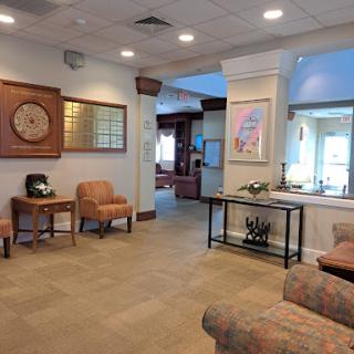 A welcoming waiting area featuring comfortable chairs and a stylish table, designed for relaxation in a well-lit lobby.