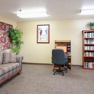 A neatly arranged office space featuring a desk with a computer, a bookshelf filled with books, and a comfortable sofa.