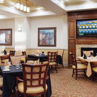 A cozy dining area with elegantly set tables and chairs, featuring a television and artwork on the walls.