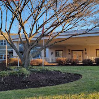 A modern building with a well-maintained lawn and tree, featuring flagpoles at its entrance.