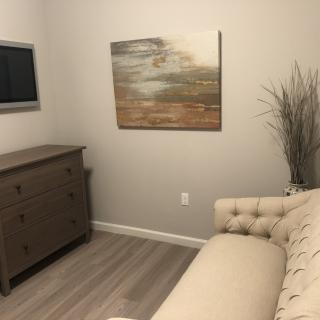 A modern living room with a sofa, dresser, wall-mounted TV, and abstract painting.