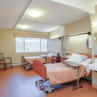 A hospital room with two patient beds and a bright window.