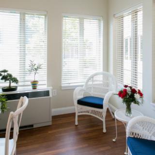 A bright and airy living room with wicker furniture, houseplants, and a bouquet of flowers on a small table.