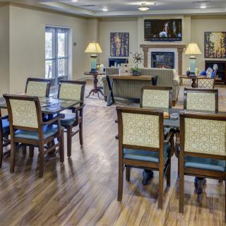 A well-lit dining area with tables and chairs, featuring wooden flooring and decorative artwork.