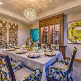 A modern dining room with a well-set table, vibrant artwork, and a stylish chandelier.