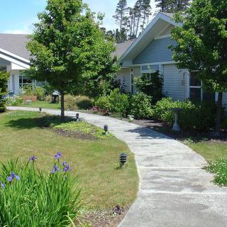 A scenic garden pathway leading to a house, surrounded by greenery and flowers.