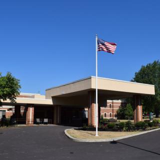 The entrance of a hospital building with a flagpole displaying the American flag under a clear blue sky.