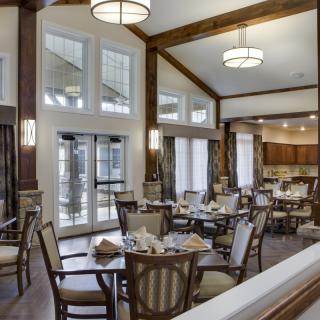 A spacious and elegant dining room with neatly arranged tables and chairs, featuring large windows and modern lighting fixtures.