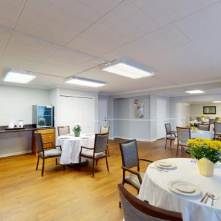 A cozy dining area with neatly arranged tables and chairs, decorated with flowers and soft lighting.