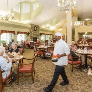 A lively dining area with seniors enjoying a meal, served by attentive staff under elegant chandeliers.