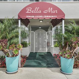 Entrance to 'Bella Mar' apartment with decorative plants and a red awning.