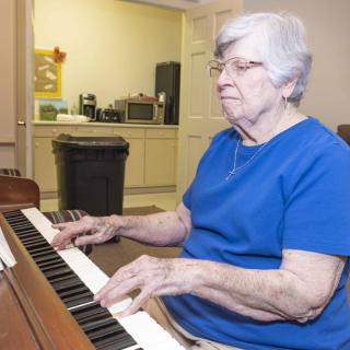An elderly woman playing the piano indoors.