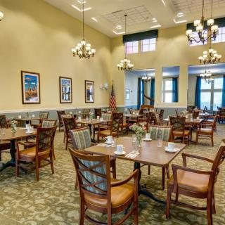 A spacious dining room with neatly arranged tables and chairs, adorned with chandeliers and decorative elements.