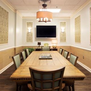 A well-lit conference room with a wooden table, chairs, and a television mounted on the wall.