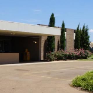 A single-story building with a driveway and landscaped greenery on a sunny day.