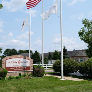 An outdoor view of a building with flags and a sign, surrounded by trees under a clear sky.