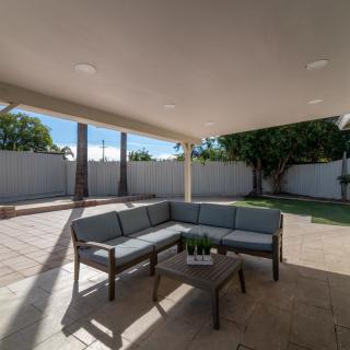 A cozy outdoor patio with a sectional sofa and table under a covered area, surrounded by a spacious backyard.