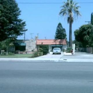 A suburban house with a driveway and a car parked under a shelter, surrounded by trees including a prominent palm.