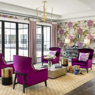 A modern living room with vibrant purple chairs and floral wallpaper, featuring elegant furnishings and large windows.