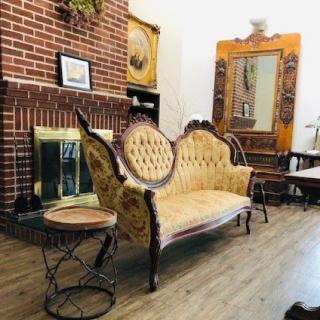 A beautifully furnished living room with a vintage sofa, brick fireplace, and antique decor.