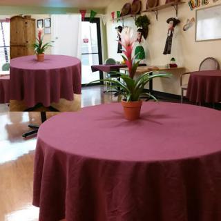 A cozy dining area featuring round tables adorned with burgundy tablecloths and decorative plants.