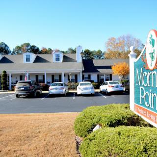 A street view of an office building with a parking lot and sign in the foreground.