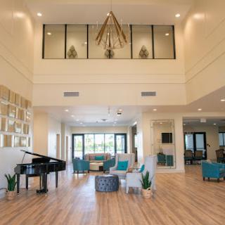 A spacious and modern lobby featuring elegant design elements, including a piano and ample seating, illuminated by natural light.